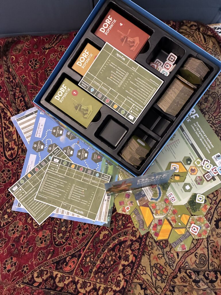 Otwarte pudełko gry dorfromantik sfotografowane z góry. Pokazany został kawałek rozłożonej gry.