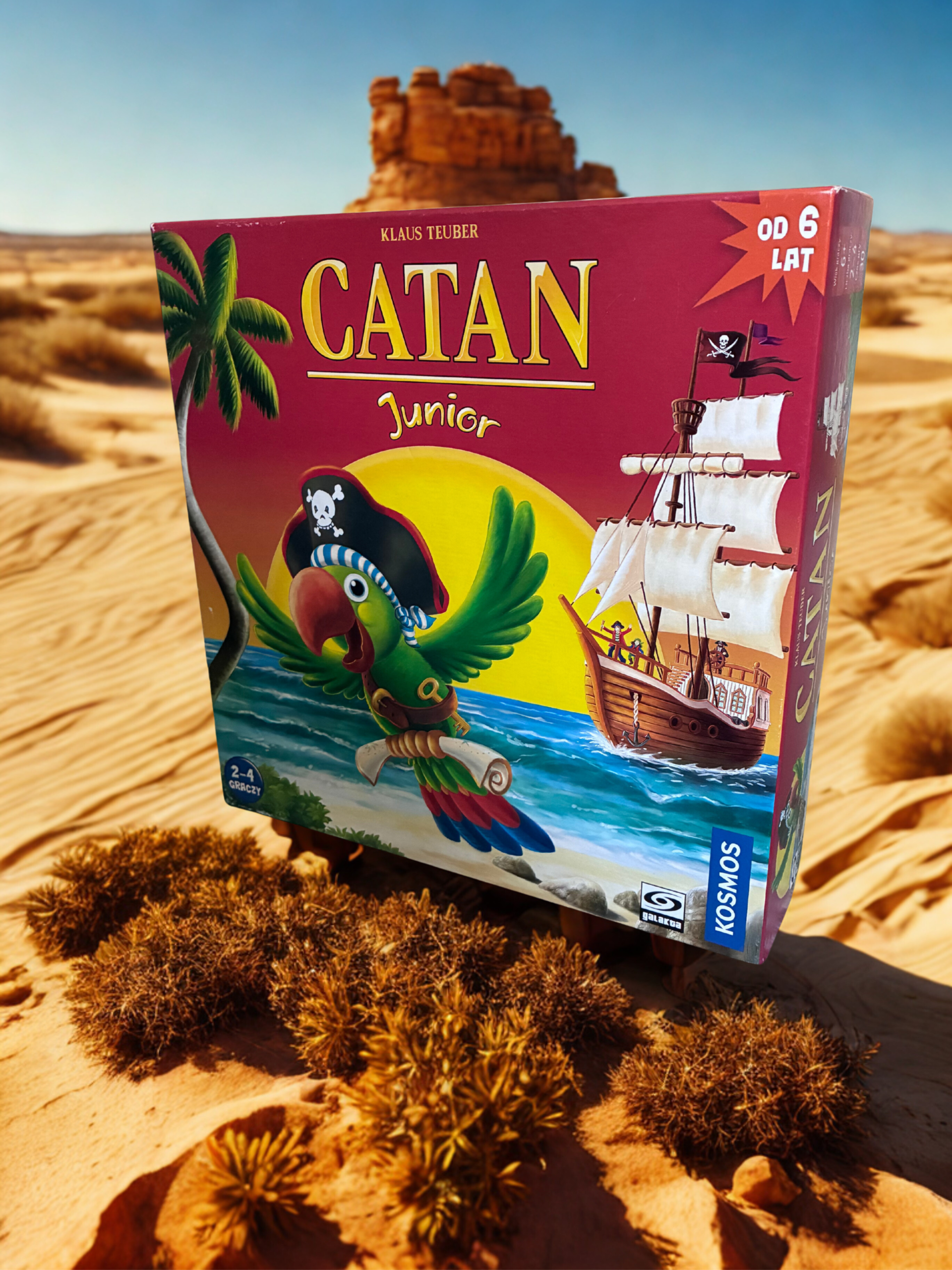 Opakowanie od gry Catan Junior na pustyni obok oazy.